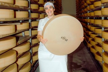 [Translate to FR (Switzerland):] Käserin im Reifekeller mit Gruyère-Käselaib in den Händern